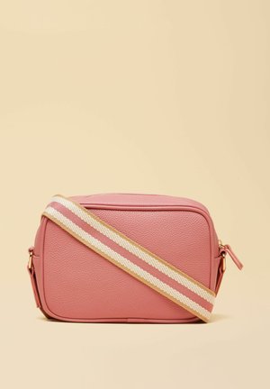 Mała prostokątna różowa skórzana torebka na ramię z beżowo-różowym paskiem na ramię o regulowanej długości na beżowym tle.