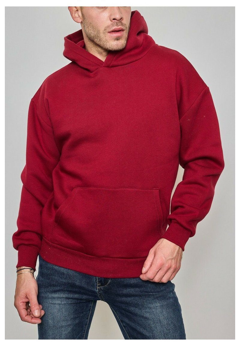 Sweat à capuche rouge en tissu doux, doté d'une poche avant, d'une capuche et de bords côtes aux poignets et à l'ourlet. Porté avec un jean bleu.