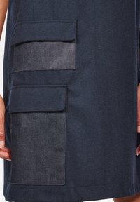 Marinblå kjol med fiskbensmönster, utrustad med två fickor med lock och en slät lapptäckningsdetalj. Skräddarsydd passform.