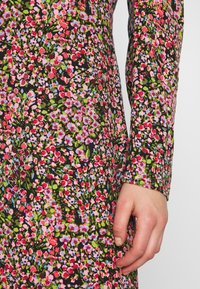 Långärmad klänning med svart bakgrund och ett livligt blommönster av rosa, röda och blå blommor, med ett mjukt, texturerat tyg.