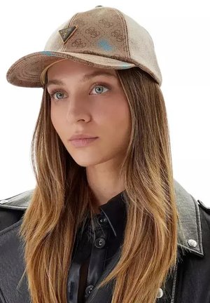 Jeune femme aux longs cheveux portant une casquette beige Guess et une veste en cuir noire, regardant légèrement sur le côté sur un fond blanc.