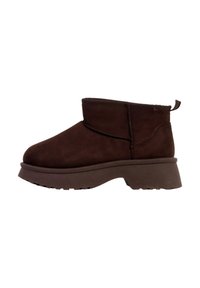 Bottes cheville en daim marron avec un bout arrondi, un panneau latéral élastique et une semelle en caoutchouc épaisse. Elles comportent une boucle à l'arrière pour faciliter l'enfilage.