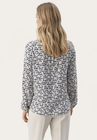 Langærmet bluse i lys blå med et geometrisk mønster af mørkeblå former. Blødt stof, rundet kant og samlede mansjetter.