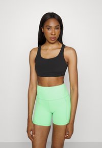 Bra desportivo preto com alças largas, combinado com calções de compressão altos de cor verde-claro. Ambos feitos de um material elástico e ajustado.