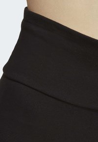 Mustat kangasvyö, jossa on pehmeä pinta ja jämäkkä, vartalonmyötäinen muotoilu. Materiaali on joustavaa ja sileää.