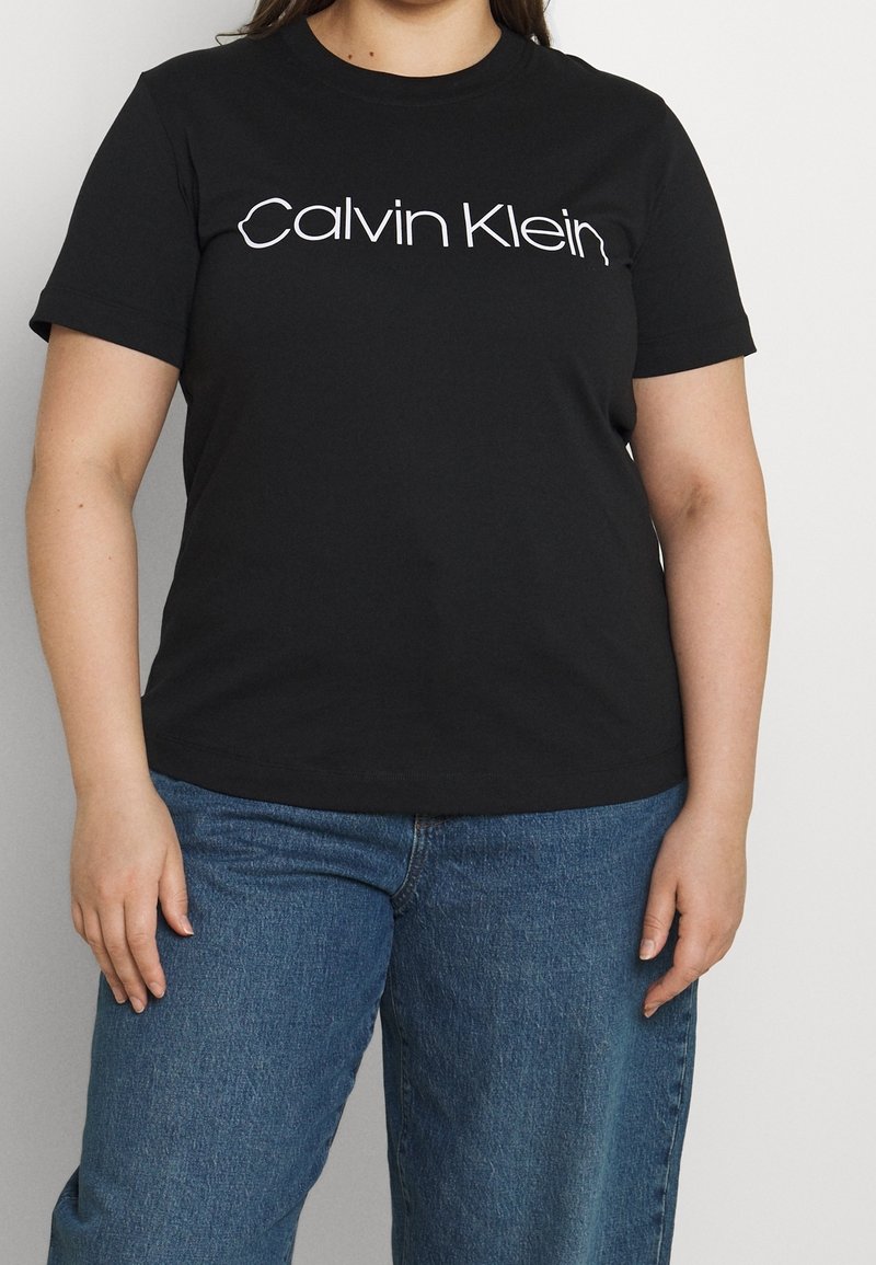 Černé bavlněné tričko s kulatým výstřihem, krátkými rukávy a bílým logem "Calvin Klein" na hrudi. V kombinaci se světle modrými džíny.