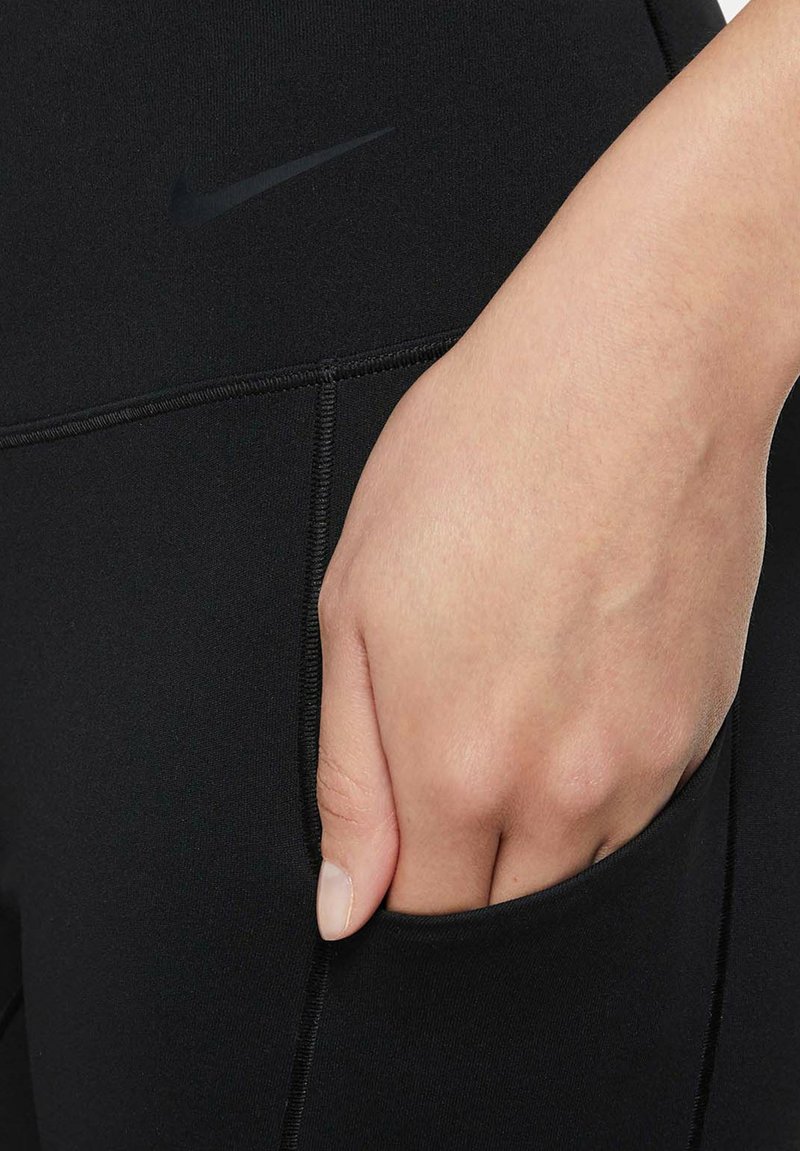Schwarze Sportleggings mit einer figurbetonten Passform, ausgestattet mit einer Seitentasche und einem dezenten Nike-Logo in Dunkelgrau. Glatte, dehnbare Stofftextur.