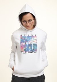 Sudadera blanca con capucha y cordones que presenta un gráfico colorido de "Alicia en el País de las Maravillas" en la parte delantera, que representa flores y paisajes caprichosos.