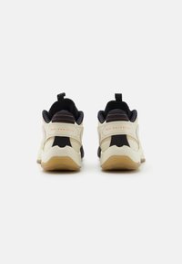 Creme- og sorte sneakers med en tekstureret overdel, polstret krave og en gummisål med en løkker. Røde accenter på hælen.