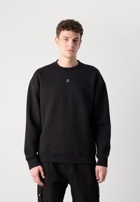 Sudadera negra con cuello redondo, puños y dobladillo acanalados. Presenta un pequeño logotipo cuadrado en el pecho. Tejido suave y texturizado.