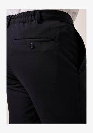 Schwarze Hose aus einem glatten, elastischen Stoff mit einem elastischen Bund und einer einzelnen, mit einem Knopf gesicherten Gesäßtasche.