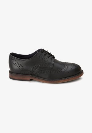 Chaussure derby en cuir noir avec un laçage, perforations décoratives et une semelle en bois brun à bout arrondi.