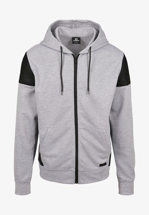 Sudadera con capucha de cremallera completa en gris claro con detalles negros de malla en los hombros, bolsillos delanteros, cremallera negra y cordones negros con puntos blancos.