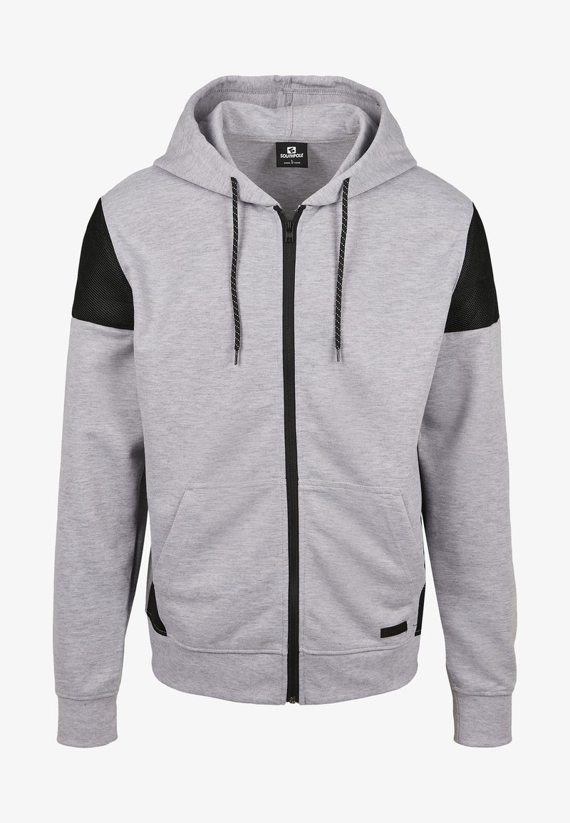 Sweat à capuche gris clair entièrement zippé, avec des accents en mesh noir aux épaules, des poches frontales, une fermeture éclair noire et des cordons noirs à pois blancs.