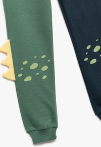 Grüne Jogginghosen mit gelben Drachenschuppen-Details und hellgrünen Flecken. Blaue Jogginghosen haben einen passenden gerippten Bündchenstoff.