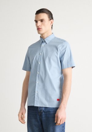 Lichtblauw kortarm shirt van zachte stof, met een button-down kraag, knopen aan de voorkant en een klein rood logo-label aan de onderrand.