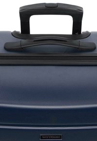 Valigia texturizzata blu navy con manico telescopico nero, zip robusta e un accento con marchio. Presenta un esterno liscio e durevole.