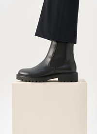 Črne usnjene gležnarske čevlje z elastičnimi stranskimi paneli, okroglo toe in teksturirano gumijasto podplat. Prikazano na nevtralnem podstavku.