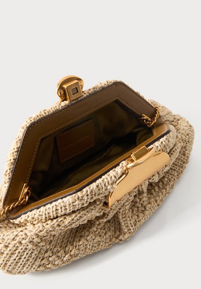 Μπεζ υφασμάτινη τσάντα με χρυσό κούμπωμα και αλυσίδα, ανοιχτή για να φαίνεται το σκοτεινό ύφασμα εσωτερικά και η ραμμένη δερμάτινη ετικέτα μέσα.