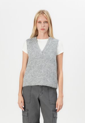 Lichtgrijze gebreide vest met een v-hals en ribbelstructuur, gedragen over een wit shirt met korte mouwen, gecombineerd met donkergrijze cargo-broek.