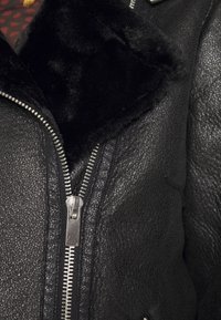 Giacca di pelle nera con finitura testurizzata, zip argentata e colletto in pelliccia sintetica nera. L'interno presenta una fodera con motivo.