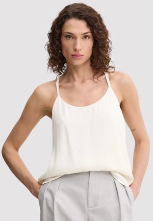 Top bianco senza maniche con spalline sottili, caratterizzato da una vestibilità comoda e una texture liscia. Abbinato a pantaloni grigi chiari.