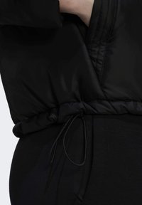 Zwarte pufferjack met een cinched trekkoord in de taille, gemaakt van glad, glanzend materiaal. Bevat een close-up van de stof en de verstelcord.
