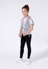 Sudadera morada sobre una camiseta azul clara con texto colorido, combinada con leggins negros y zapatillas blancas con detalles morados.