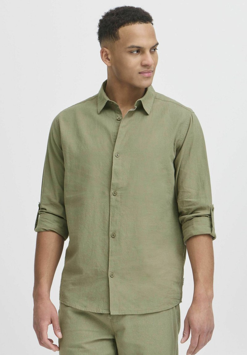 Light olive green, long-sleeved shirt in a linen blend, featuring a collared neck, button closures, and rolled sleeves. Smooth texture.