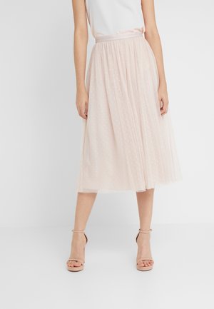 Jupe midi en tulle rose clair avec un motif à pois et une taille élastique, portée avec des talons à bride beige. Texture lisse, design superposé.