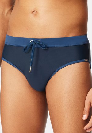 Mann trägt dunkelblaue Badehose mit einem hellblauen Taillenbund und Frontkordelzug.