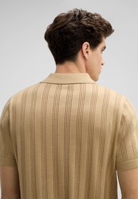 Beige polo shirt met korte mouwen, voorzien van verticale strepen en een textuurpatroon. Ribgebreide kraag en mouwen. Platte naden, lichtgewicht breimateriaal.