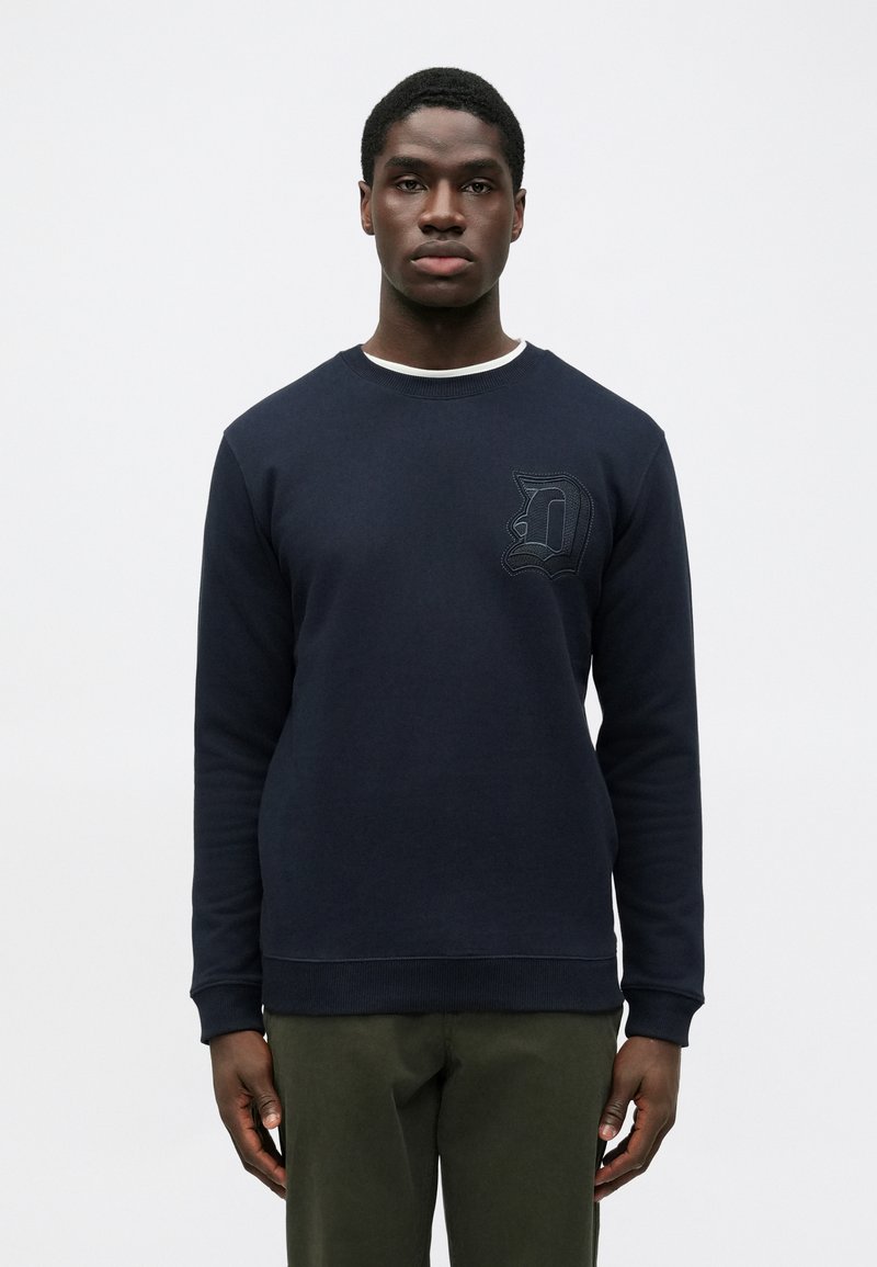 Marineblå sweatshirt med rund halsudskæring, lange ærmer og ribbede manchetter. Har et struktureret 'D' logo på brystet. Materialet er en bomuldsblanding.