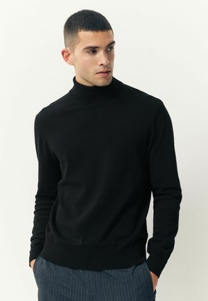 Zwarte coltrui gemaakt van een gladde stof, met lange mouwen en een getailleerde pasvorm, gecombineerd met gestreepte broek.