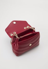 Borsa a mano in finta pelle rossa con motivo trapuntato, hardware in tono oro, tracolla a catena e tasca interna con zip. Flap esagonale aperto.