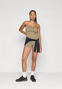 Καφέ κοντό τοπ και ταυτισμένα ψηλόμεσα σορτς, με ναυτικό μπλε πουκάμισο δεμένο. Το μοντέλο φοράει μαύρα αθλητικά παπούτσια και άσπρες κάλτσες. Λείο υφασμάτινο υλικό.