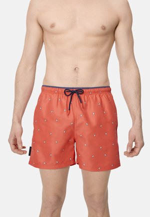 Torso masculino con pantalones de baño coral con pequeños dibujos de pingüinos blancos y un cordón azul marino sobre un fondo liso.