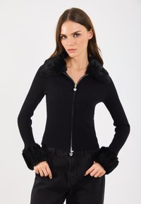 Czarna, prążkowana kurtka zapinana na zamek, z sztucznym futerkiem przy kołnierzu i mankietach, z detalem zamka w kolorze srebrnym, dopasowany fason, noszona z czarnymi spodniami z wysokim stanem.