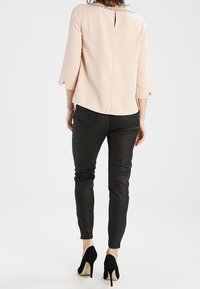Blusa rosa con maniche a 3/4 e sottile spacco posteriore, abbinata a pantaloni neri aderenti e scarpe con tacco alto nere. Tessuto dalla consistenza liscia.