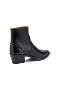 Botín negro de cuero hasta el tobillo con puntera afilada, tacón pequeño y acento de tachuelas en la parte trasera. Textura suave con cremallera lateral.