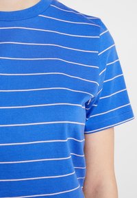 Niebieska bawełniana koszulka z poziomymi różowymi paskami, okrągłym dekoltem i krótkim rękawem; gładka faktura o swobodnym designie.