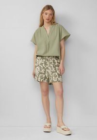 Blusa corta a maniche corte verde oliva con scollatura a V; pantaloni shorts crema con motivo floreale; sandali con platform con cinturini larghi e dettagli testurizzati.