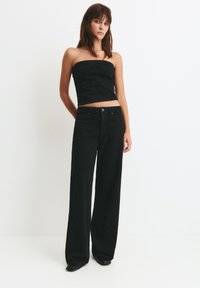 Čierny denimový outfit s topom bez ramienok a širokými nohavicami. Tkanina má jemný lesk, doplnený priliehavým strihom a čistými líniami.