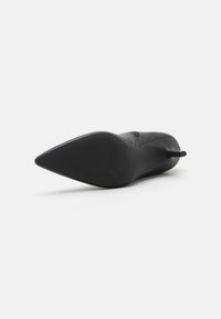 Zapato de tacón alto negro con punta afilada, textura suave y una silueta elegante. Presenta una suela de goma con ranuras horizontales para mayor agarre.