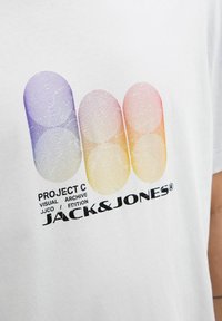 Hvid bomulds t-shirt med et glat, flerfarvet grafik af tre overlappende cirkler i lilla, pink og orange, med sort tekst nedenfor.