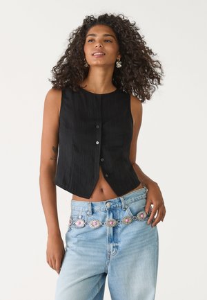 Black sleeveless top with a button front, paired with light blue jeans featuring a decorative silver and pink belt. Smooth texture and fitted shape.