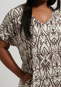 Koszulka z dekoltem w serek i krótkim rękawem w kolorze kremowym z ciemnobrązowym wzorem kwiatowym. Miękka tkanina o luźnym kroju, z kieszenią w szwie bocznym.