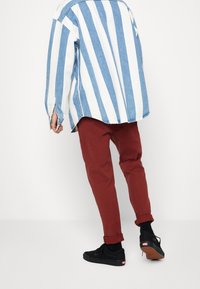 Camisa vaquera con rayas azules y blancas, combinada con pantalones rojos ajustados y zapatillas negras. Los pantalones están doblados en los tobillos.