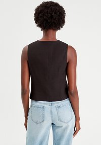 Haut noir sans manches avec une coupe droite, coutures minimales à l'arrière, associé à un jean taille haute bleu clair.