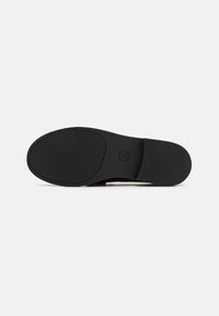 Semelle d'une chaussure habillée noire avec des sections antidérapantes texturées, un bout arrondi, un talon plat et le logo "Michael Kors" sur la zone avant-pied.